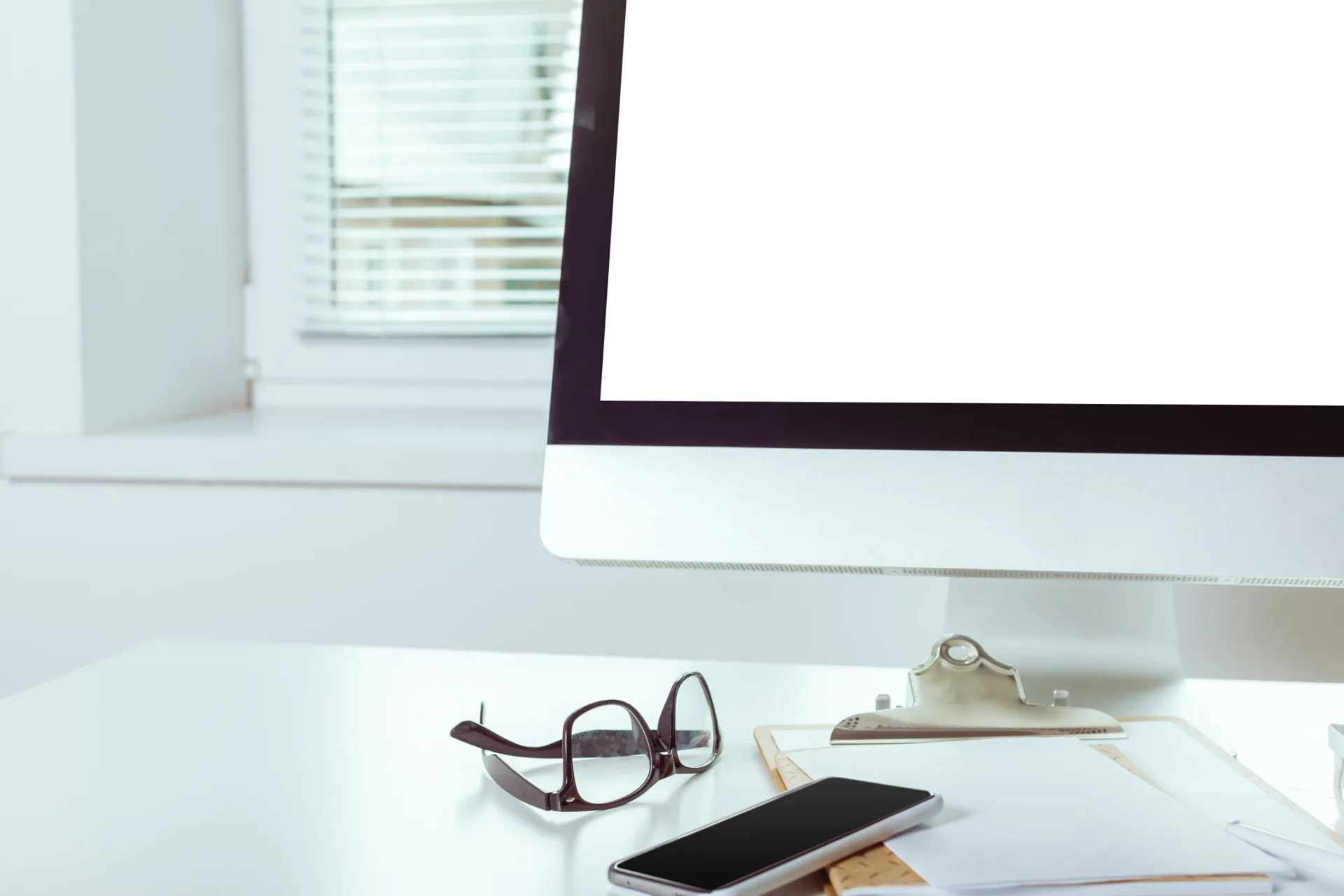 Heller Arbeitsplatz mit Bildschirm, Brille und Smartphone am Fenster