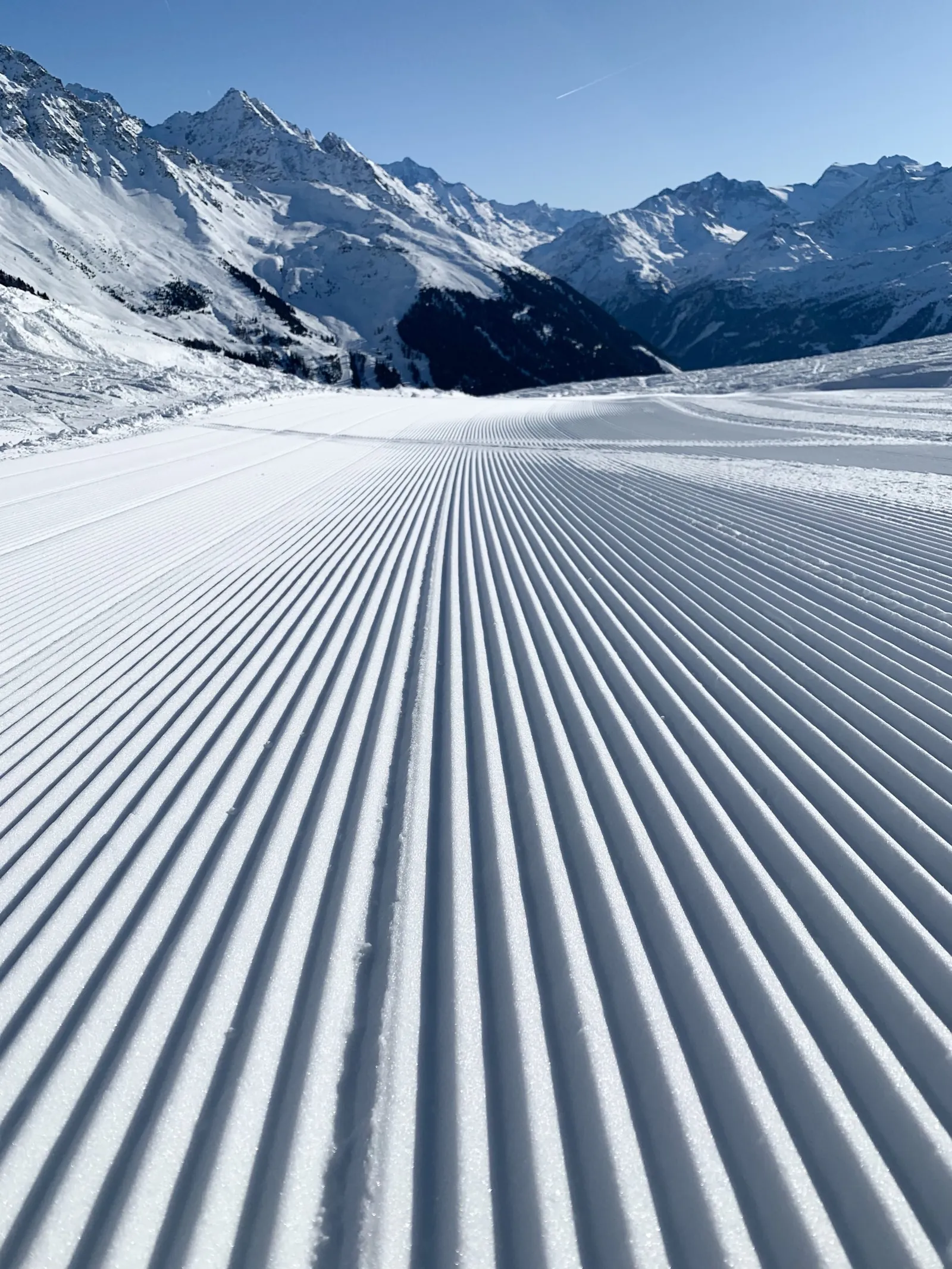 Frisch präparierte Skipiste vor verschneiten Alpengipfeln